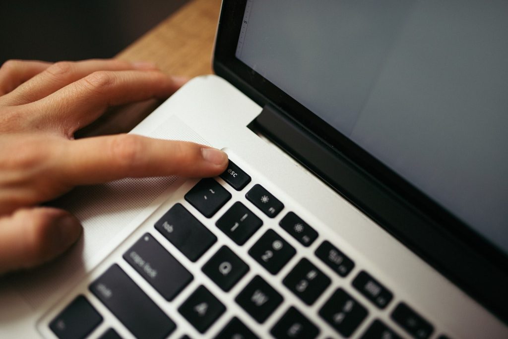 A hand rests on a laptop keyboard, pressing a key. The workspace is minimalistic, emphasizing the act of typing. Soft lighting highlights the sleek design of the laptop.